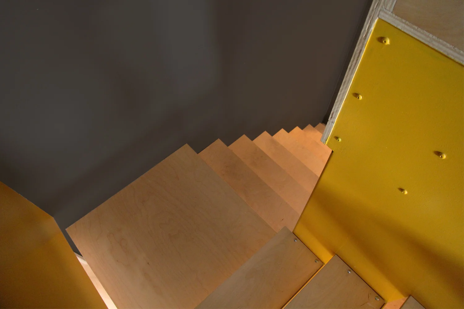 Nouvel escalier en acier peint jaune suspendu à l’étage. Contremarche ouverte et marche en bois. 2ieme section de marche intégrée à un meuble de rangement en bois.