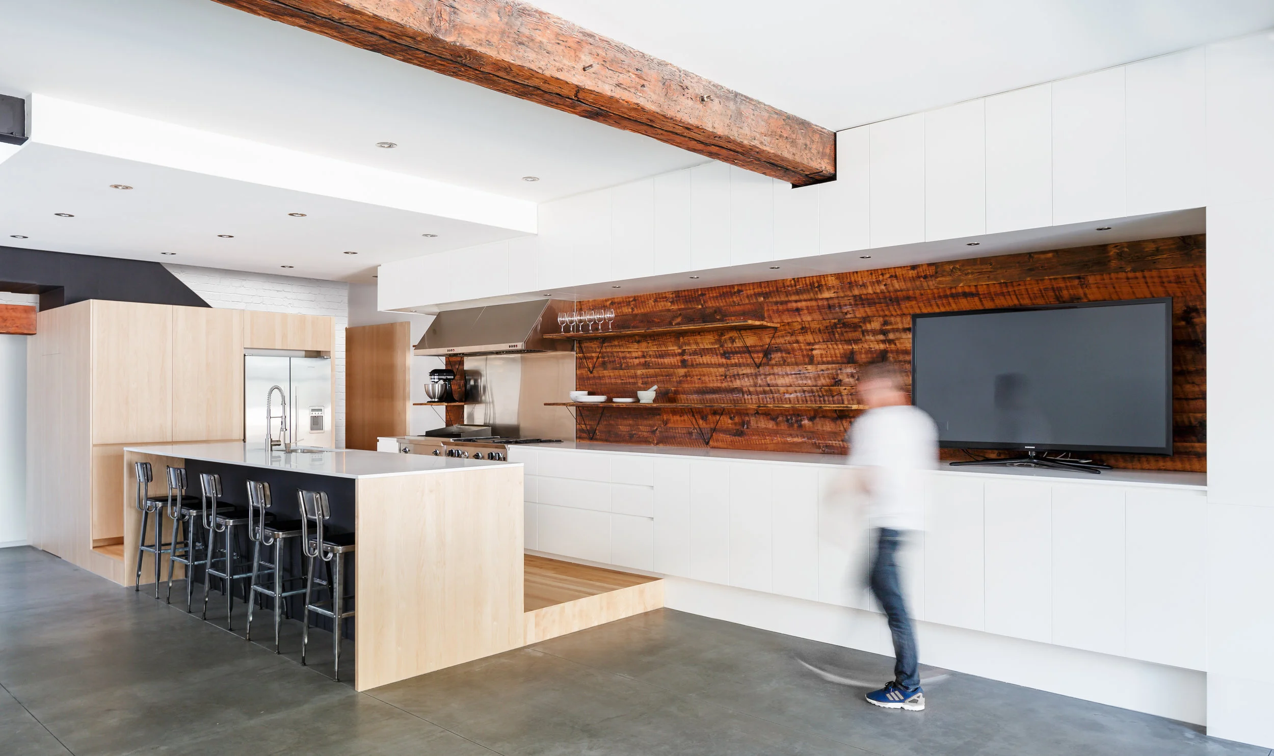 Renovation of kitchen. Storage block under the stairs. Built-in refrigerator. Island with bar height counter in white quartz. Another view of the railing of the black metal staircase