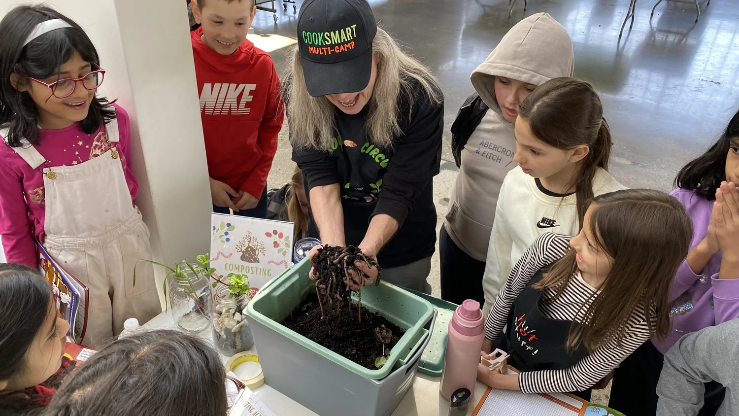 A woman demonstrating how to compost worms to a group of children gathered around a table.