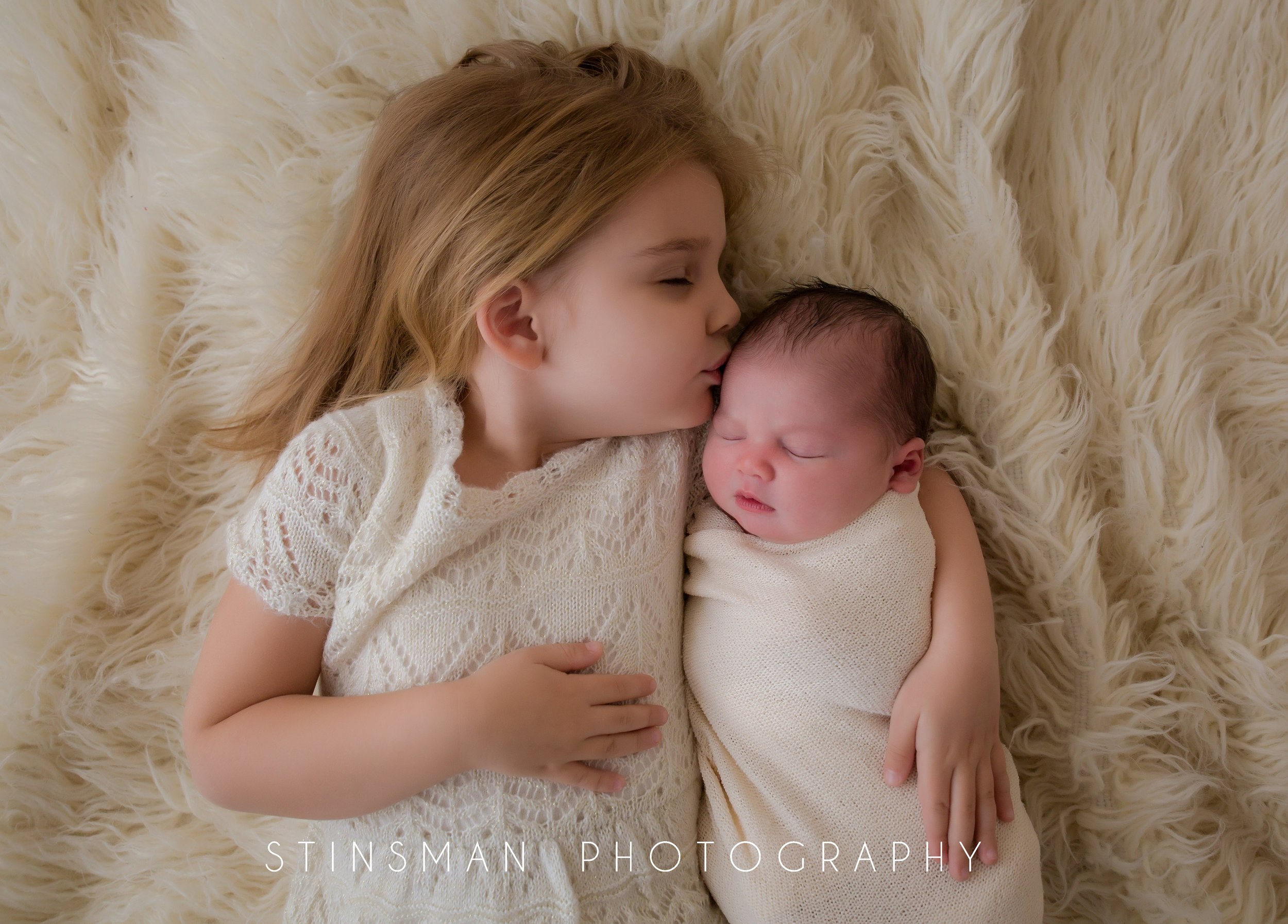 little girl kissing her baby sister while laying on a white rug