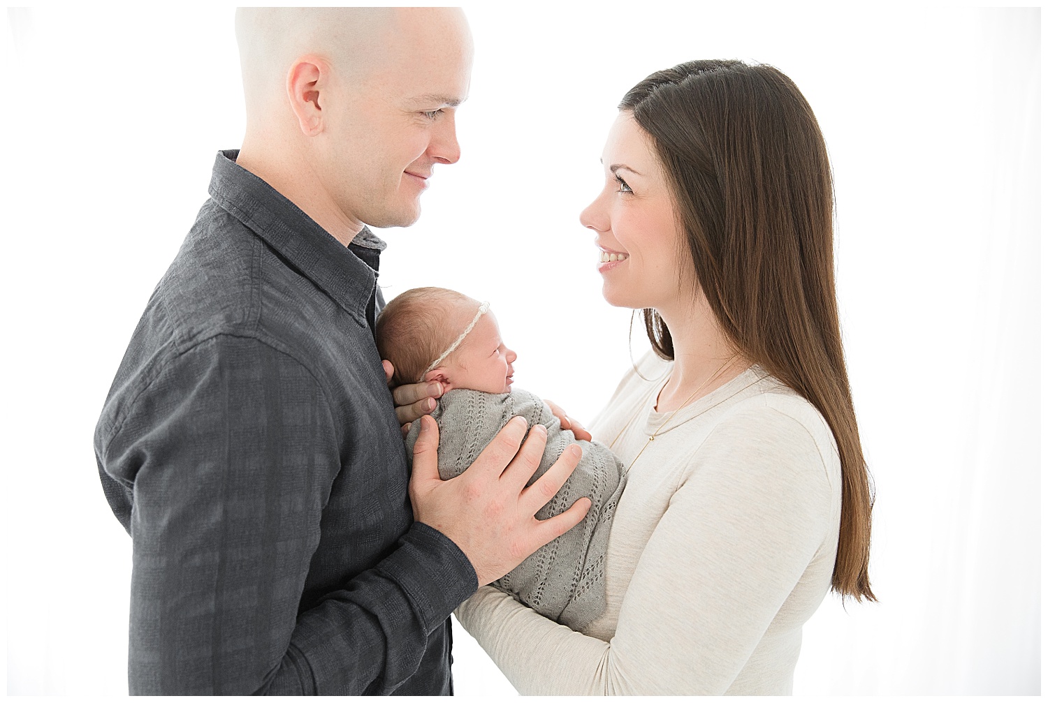 baby smiling at her mom while dad holds her tightly in burlington new jersey photo studio