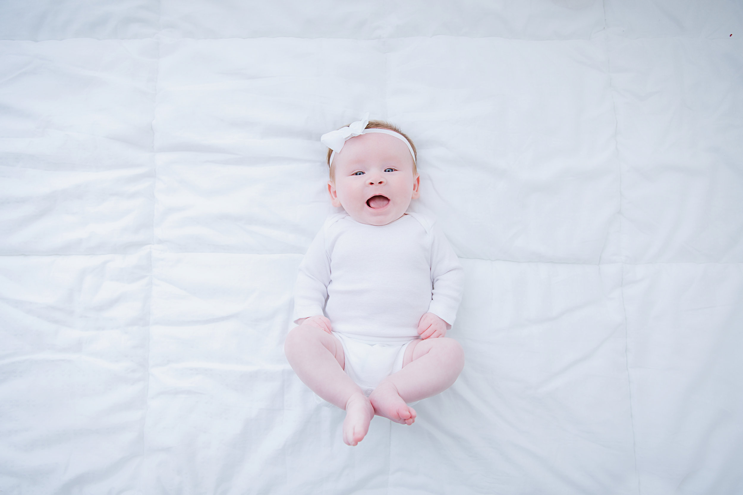 smiling-baby-girl-looking-at-camera-white-bed-white-clothes-photography-shoot-new-jersey