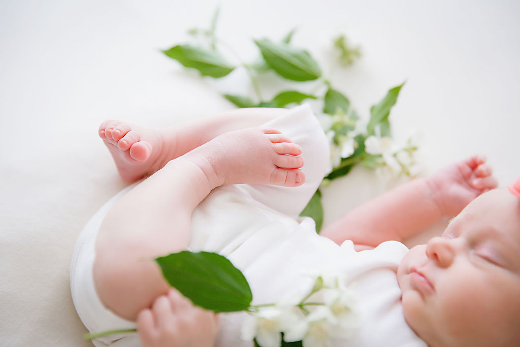 A newborn baby girl lying by some greenery in a photography studio. Taken by a newborn photographer in Burlington New Jersey.