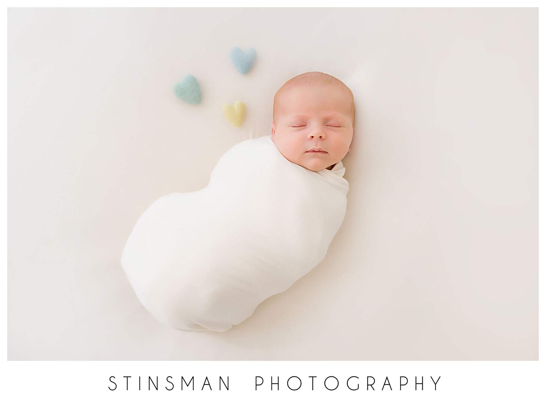 newborn-baby-boy-wrapped-in-cream-with-blue-yellow-and-green-hearts.jpeg