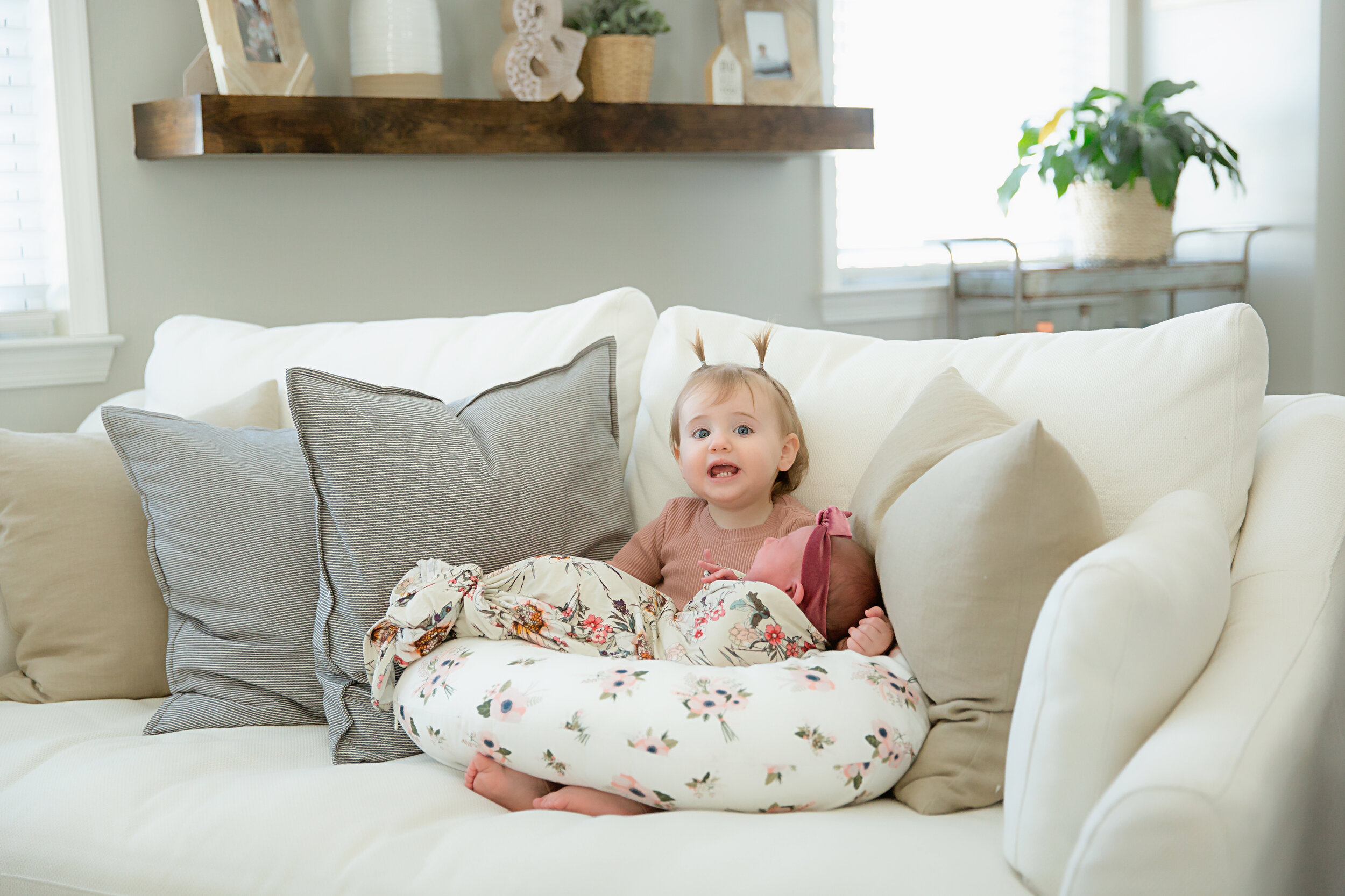 big-sister-holding-baby-girl-on-white-couch-in-deptford-home-newborn-session.jpeg