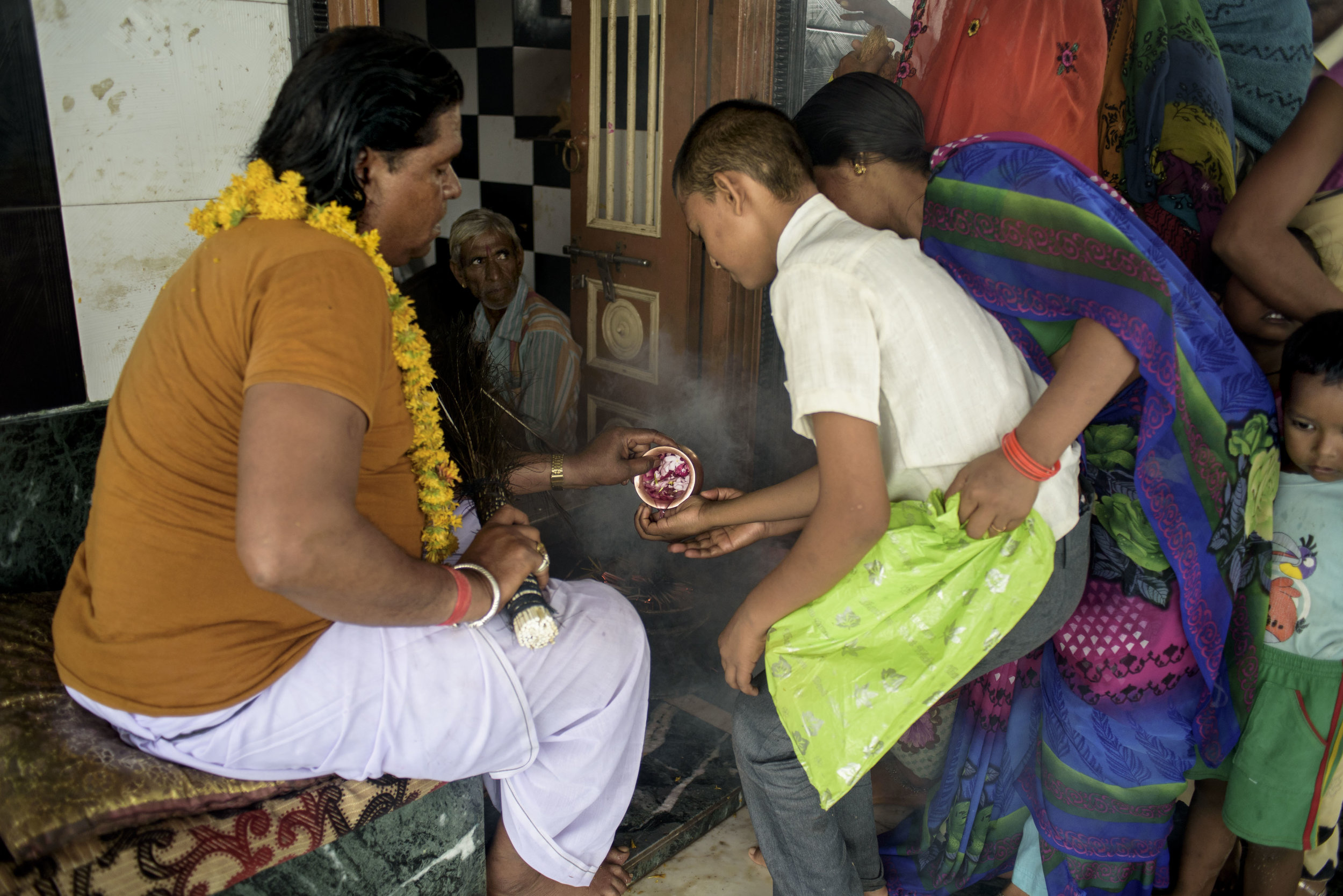 A young boy takes the blessings of the head Bhopa. The people come in thousands to perform weekly rituals and offer a sum of money, fruits, garlands. People wait in a long queue to meet the head Bhopa and taste the holy water given by him.