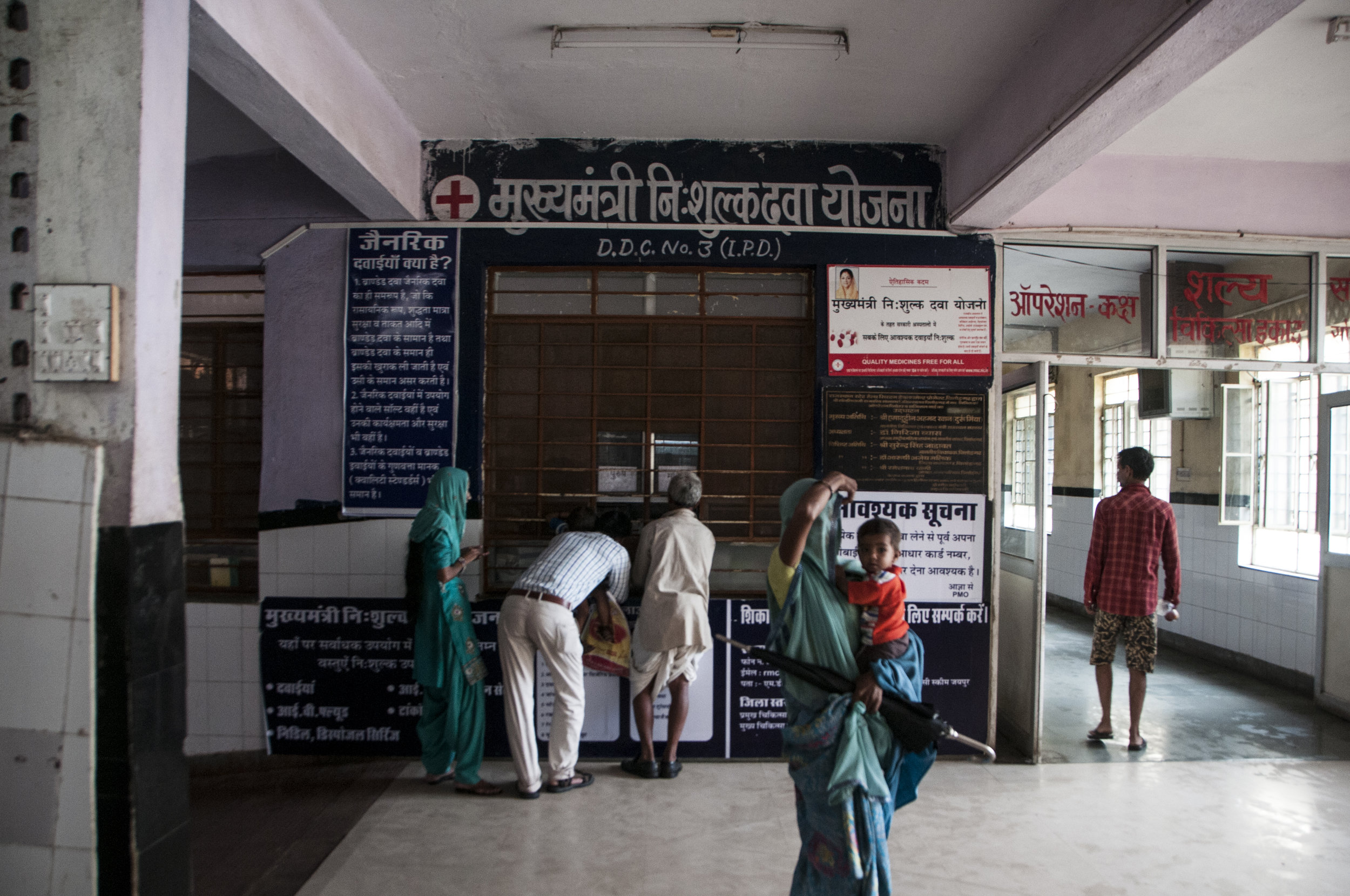Patients outside the District Drug Center (DDC) No.3 of Chittorgarh’s District Hospital on a day of unusual calmness, after days of flash floods. This hospital houses 8 DDCs, and multiple Lifeline counters where patients can obtain generic medications that are not on the Essential Drug List of over 500 items.