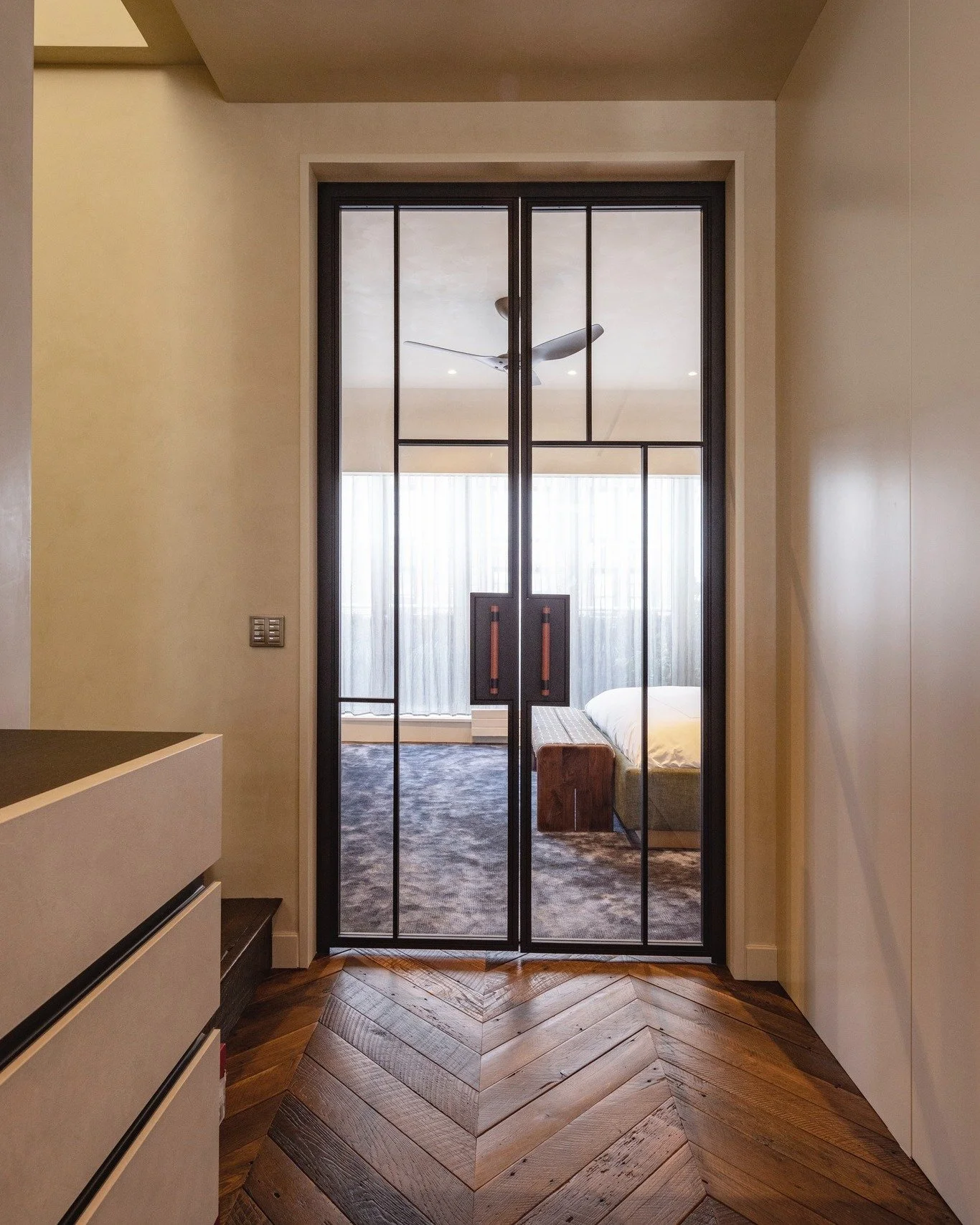 The bedroom at our SoHo Duplex opens through a custom steel-and-glass door, its leather pulls mounted on black steel backplates. The leather appears again on the built-in wardrobe pulls, part of the extensive custom millwork throughout this rooftop p