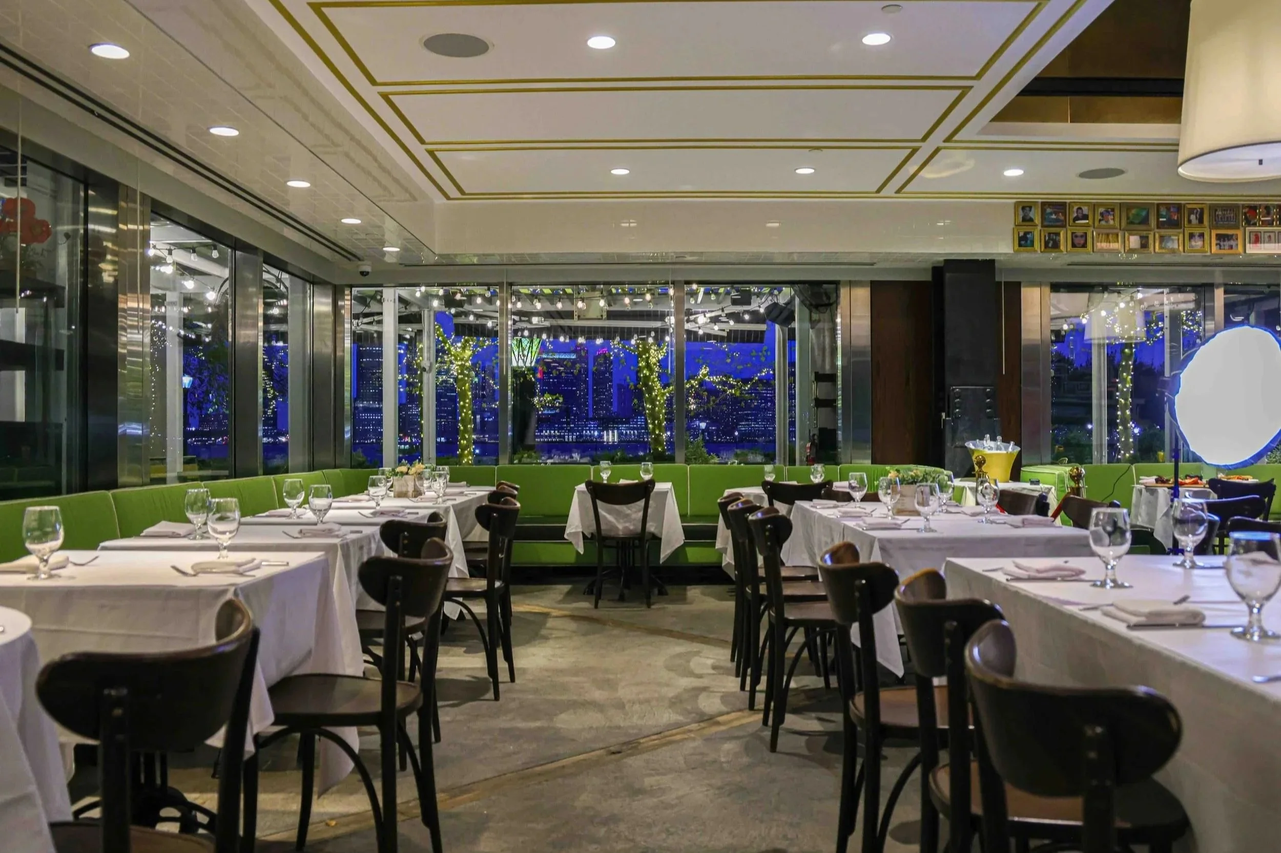 The bistro dining room at night: white-clothed tables, dark wood chairs and green banquettes by tall windows.