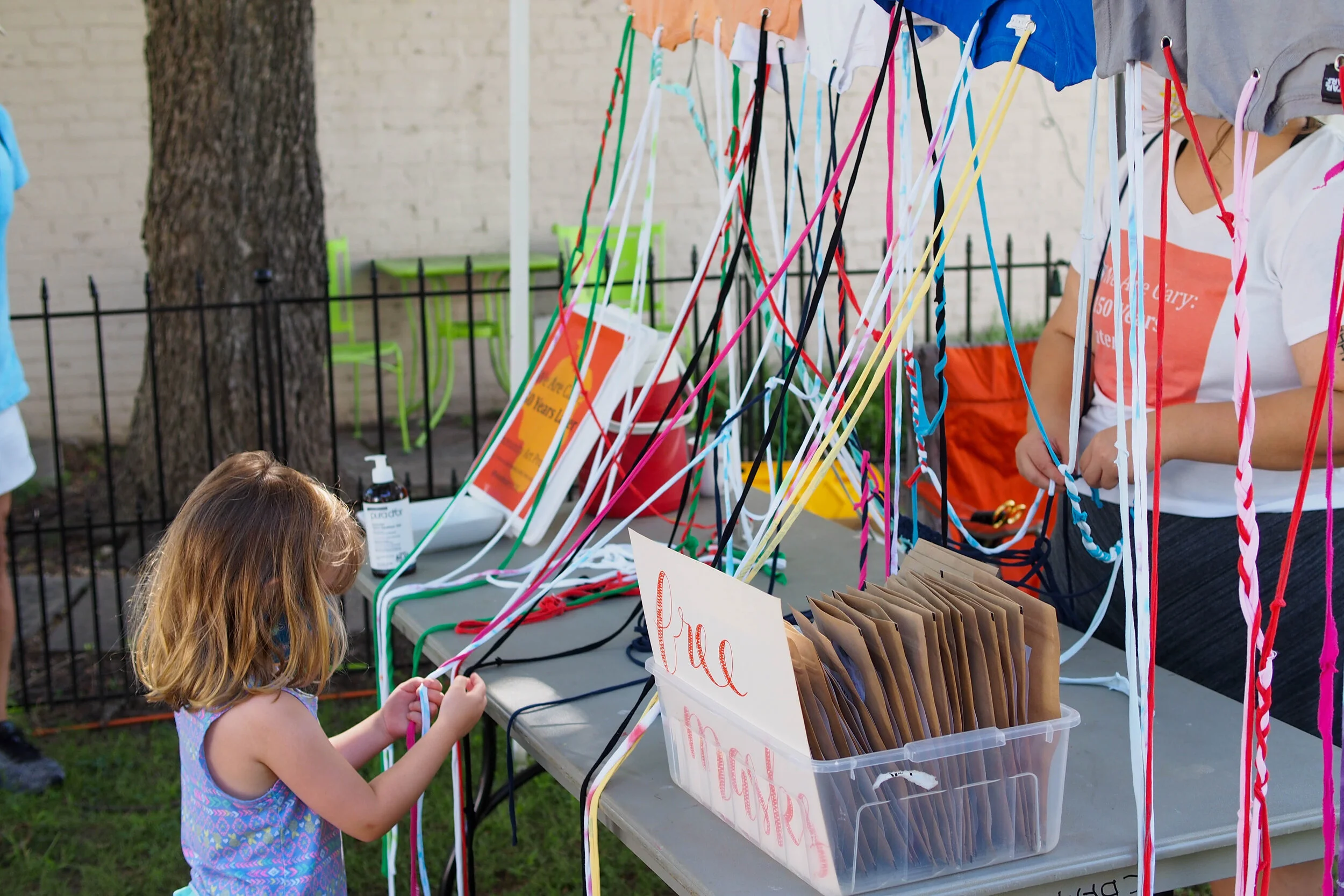 Young girl braiding t-shirt rope at the Cary Downtown Famers Market booth.