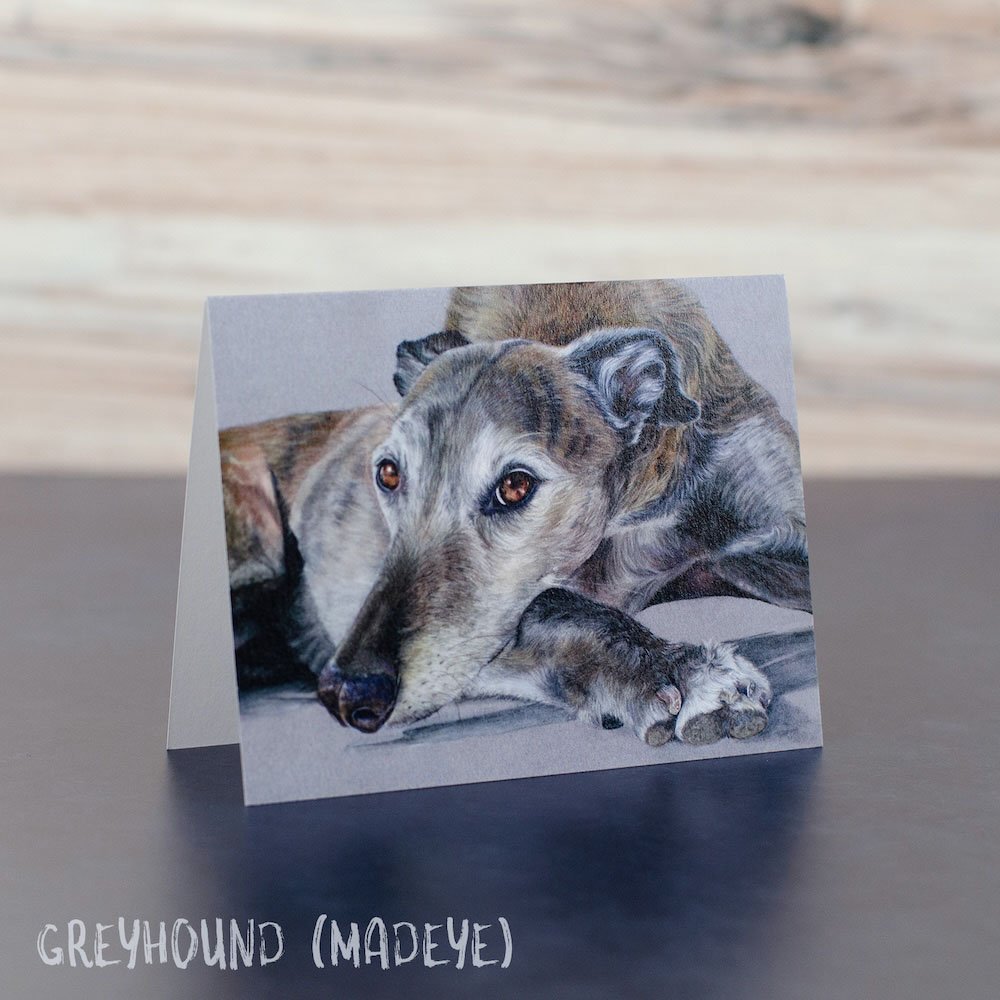 Pastel drawing of a brindle greyhound lying down and looking at the viewer. Art is shown printed on a blank greeting card.