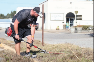 Todd Burney trims tall weeds and grass in front of the Columbus County Arts Council Saturday morning.