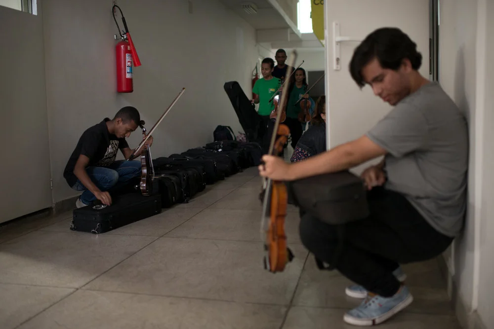 Dez. 5, 2017. Ao fim do ensaio de três horas, os alunos guardam os instrumentos do projeto em cases que ficam organizados no chão do lado de fora da Sala de Ensaio. Felipe Silva, 17 anos (à direita na foto), é considerado um aluno promissor: em janeiro de 2017, tirou 10 na UNIRIO, além de outras 9.7 e 9 no curso de licenciatura em música. Em seus planos estão um intercâmbio, bacharel e doutorado em música.
