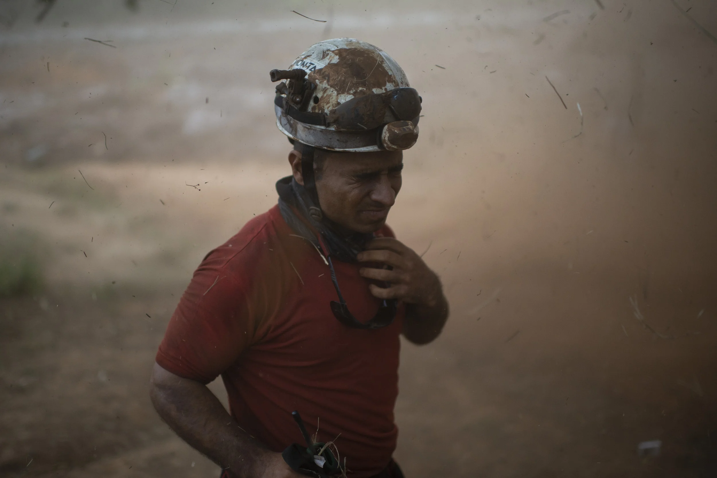  A firefighter protects himself while a helicopter lands on a site to rescue a body that was found in the mud, in Parque das Cachoeiras, Brumadinho. 2019 © FOR BBC NEWS BRASIL 