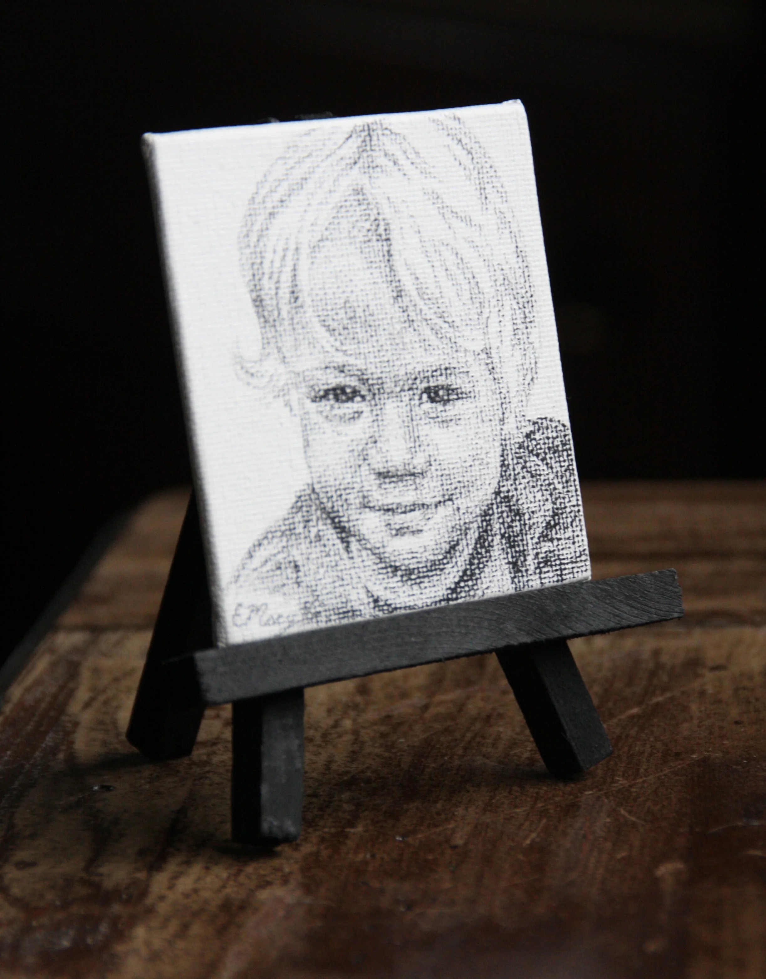 A 3x3 inch charcoal portrait with a black easel perfect for display.