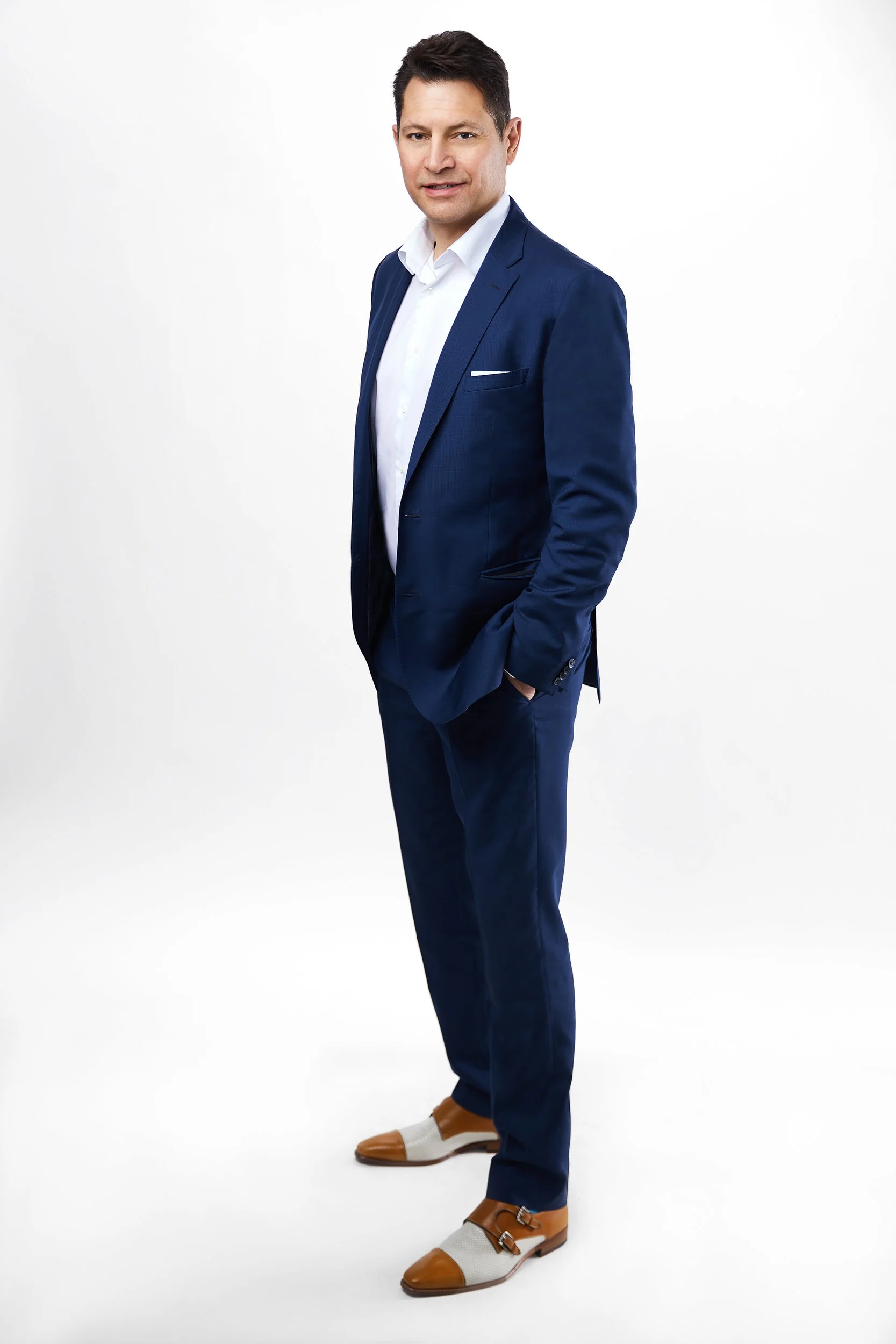 Man in a navy suit with white pocket square, full-body business portrait against a white background.