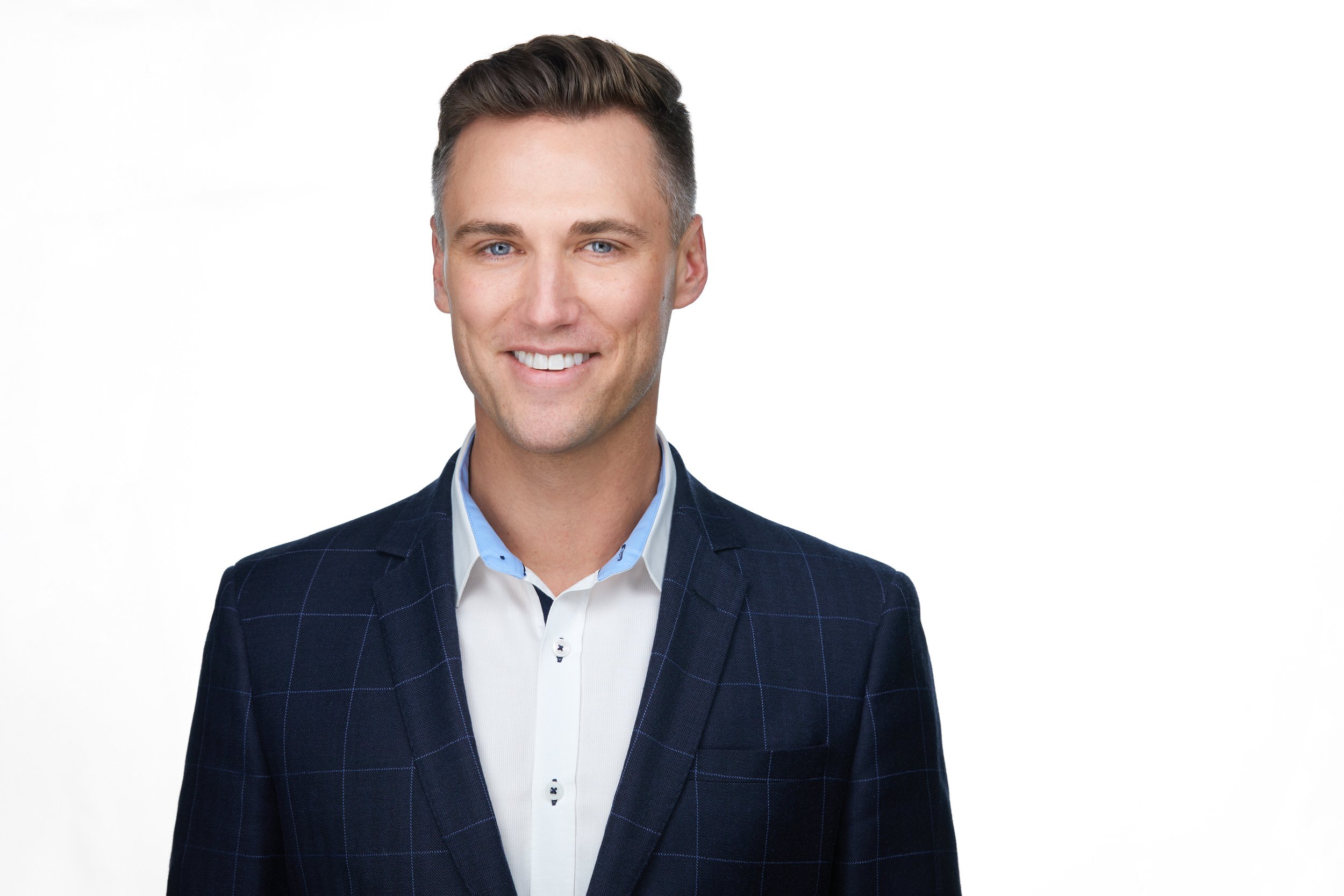 Man with brown hair in a navy checkered blazer and white shirt, smiling corporate headshot against a white background.
