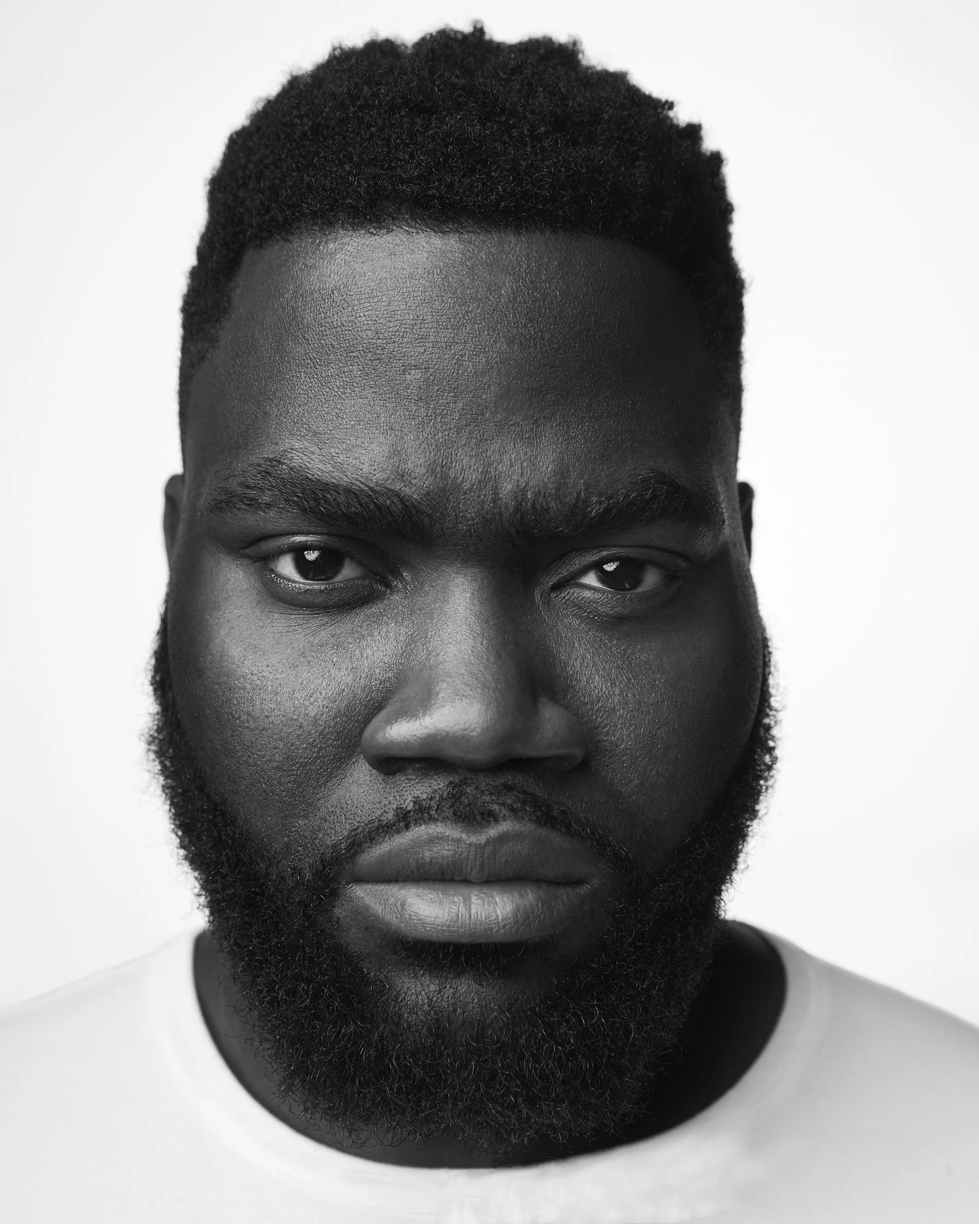 Black-and-white close-up portrait of a man with a full beard, serious expression against a white background.