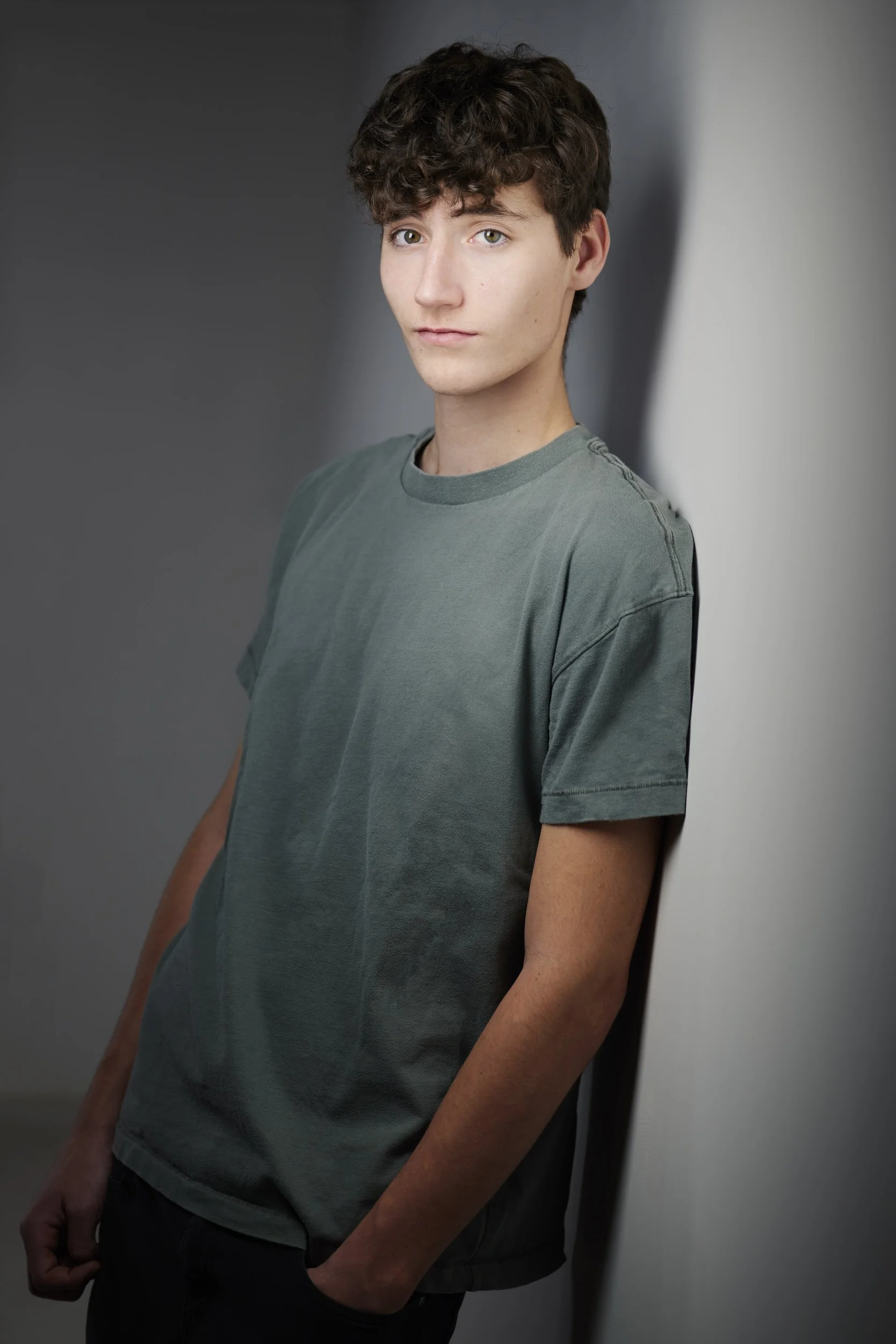 Young man with curly brown hair in a grey t-shirt, headshot against a grey background.