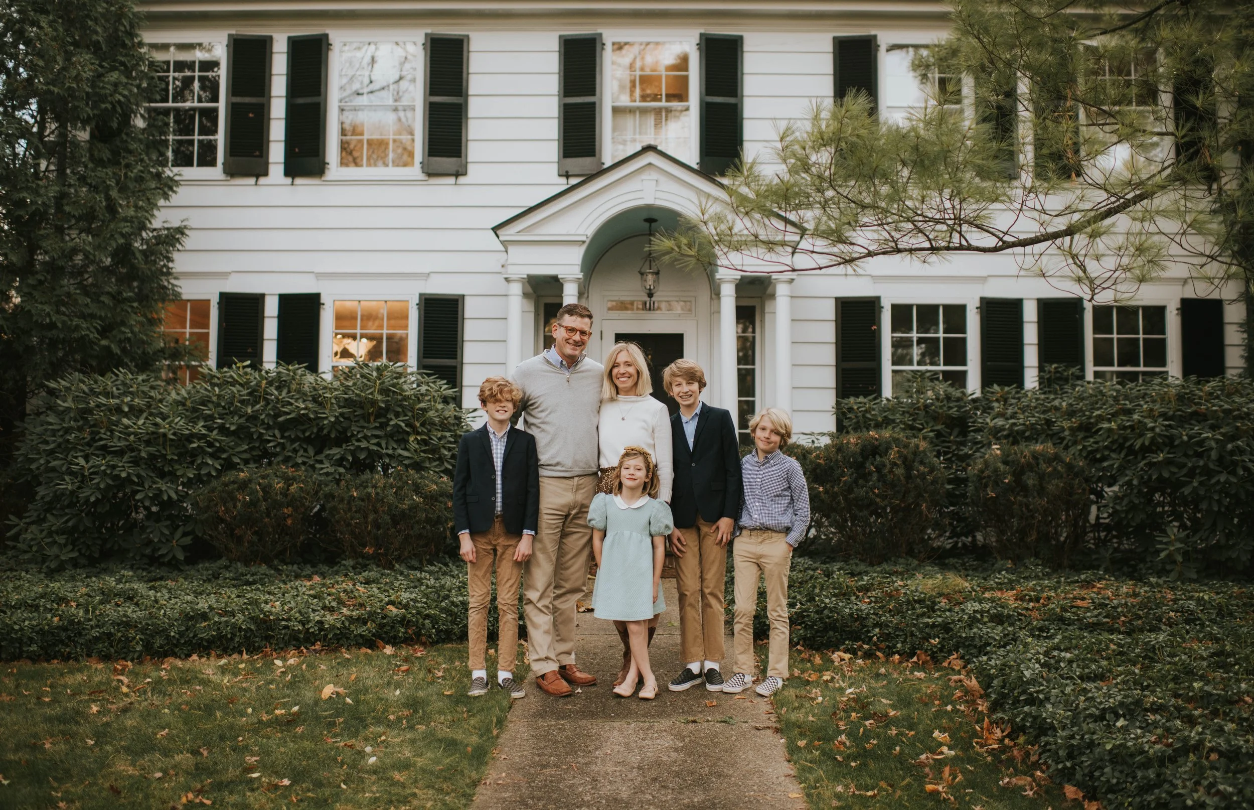 family poses in front of white house with black shutters