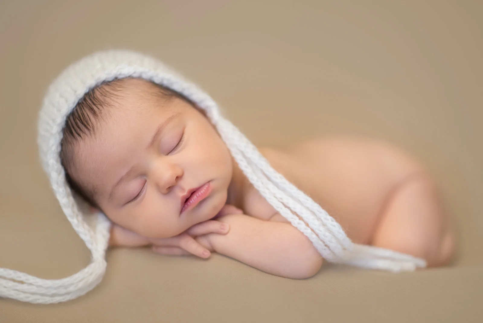  Newborn baby with white bonnet on mocha background 