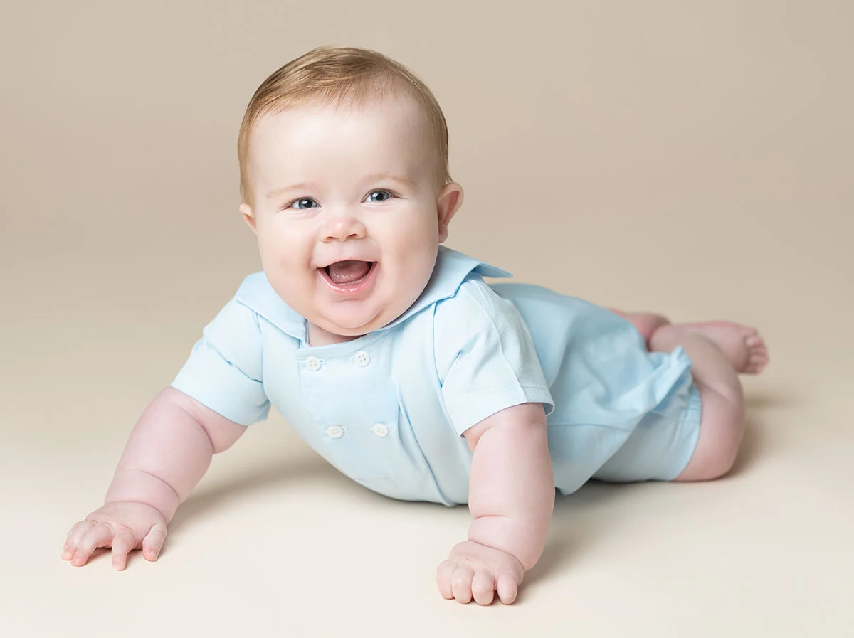 Portrait of a smiling baby boy in a blue outfit on a cream background