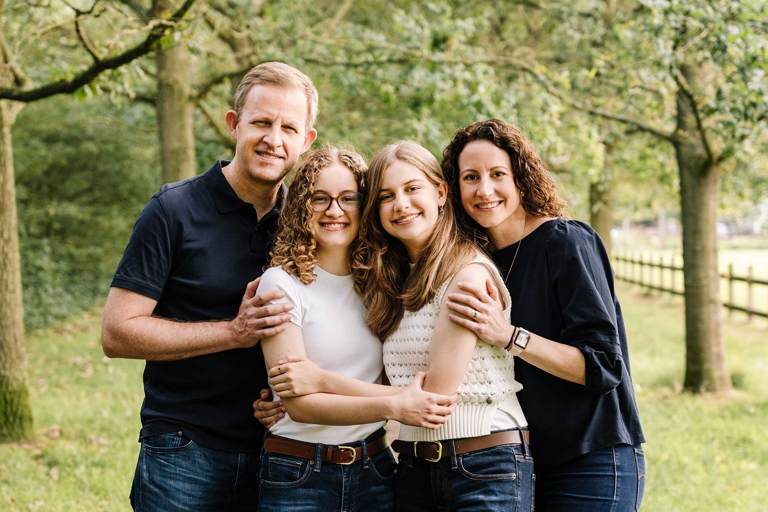 Parents hugging their teenage daughters under a path of trees at Clingendael park. 