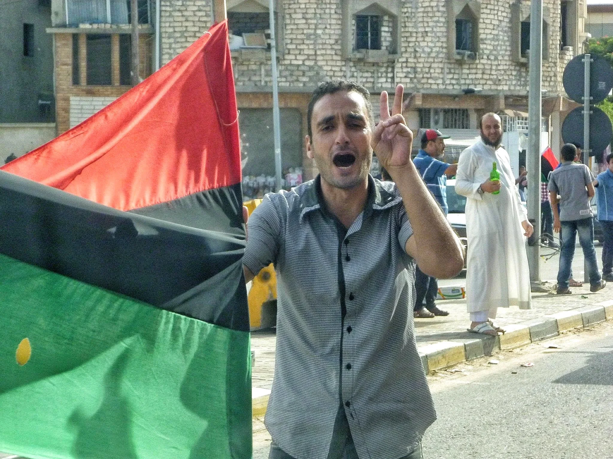 Man holding a Libyan flag and making a victory sign — Tripoli, 20 October 2011