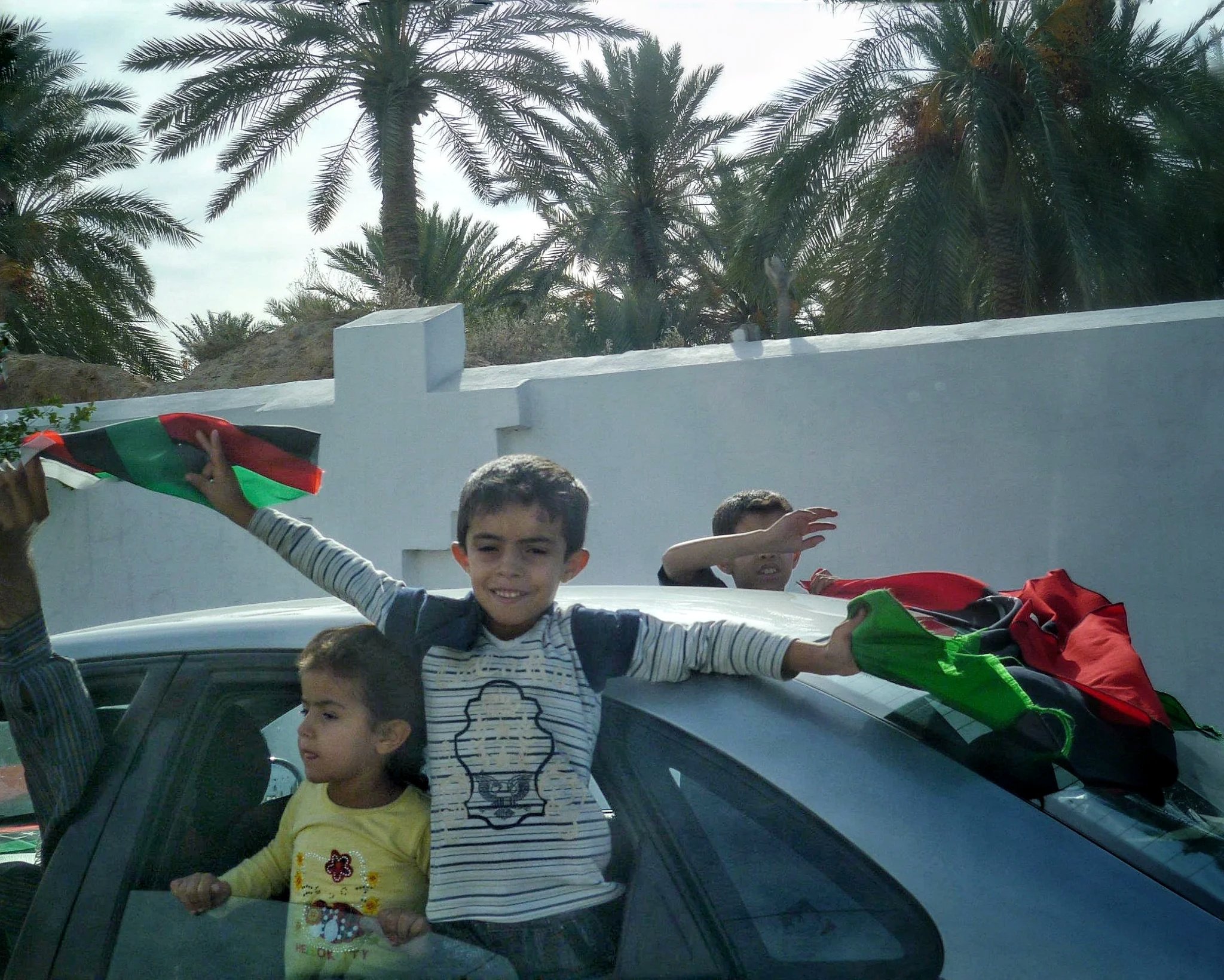 Children with Libyan flags beside palm trees — Tripoli, 20 October 2011