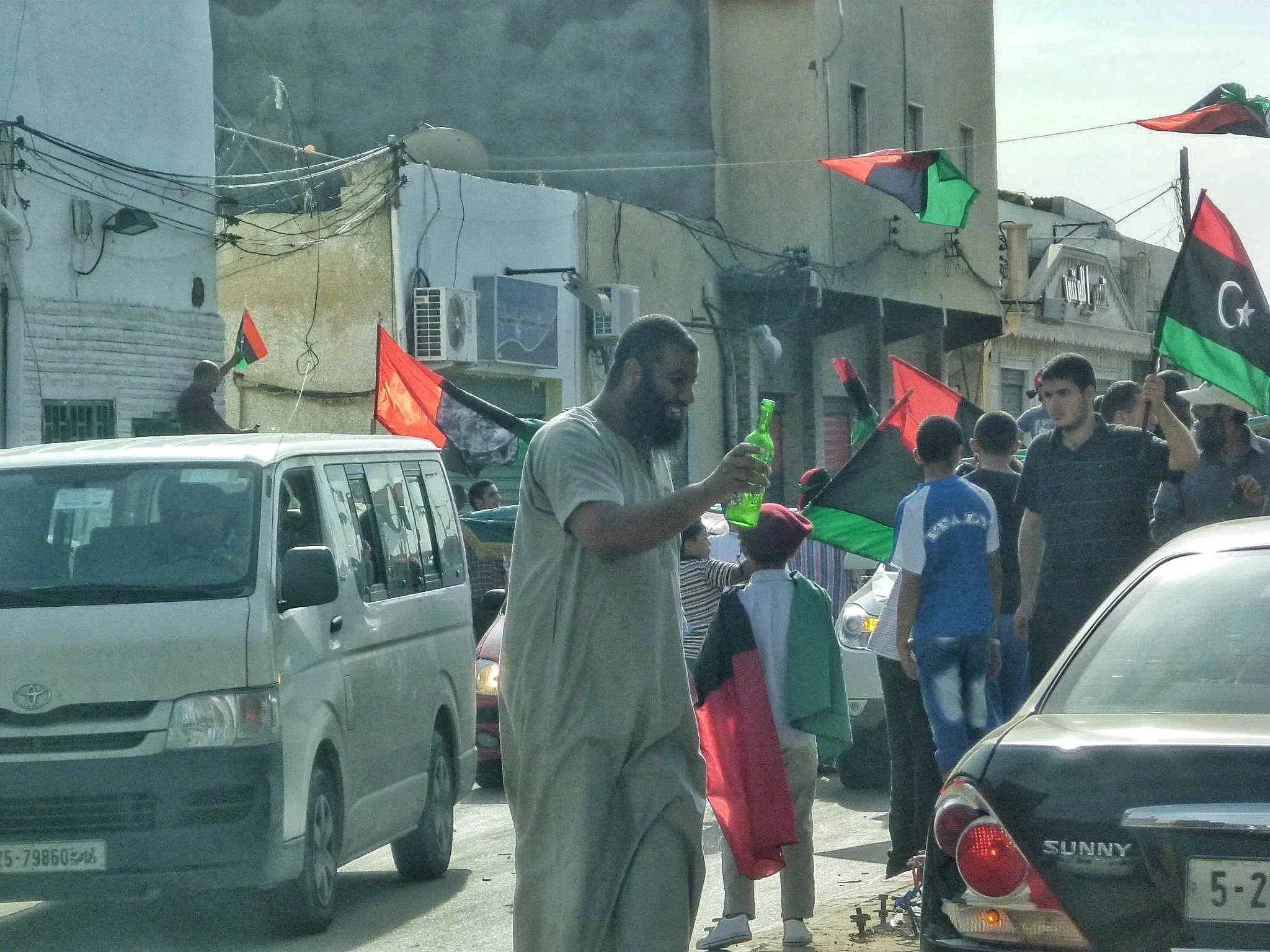 Man in a grey robe among a street procession — Tripoli, 20 October 2011