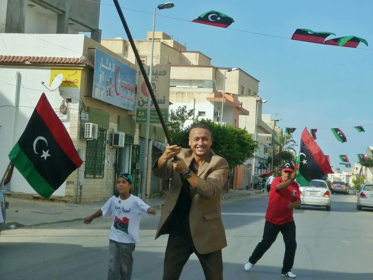 Man waving a Libyan flag beneath street bunting — Tripoli, 20 October 2011
