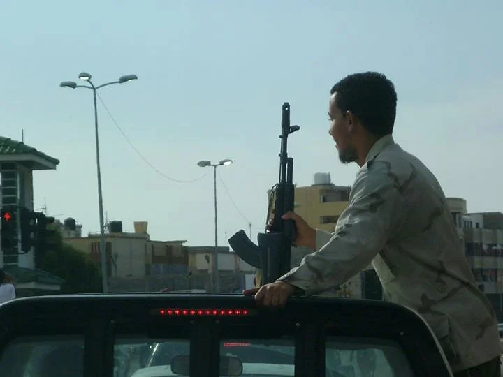 Man holding a rifle while riding on a vehicle — Tripoli, 20 October 2011