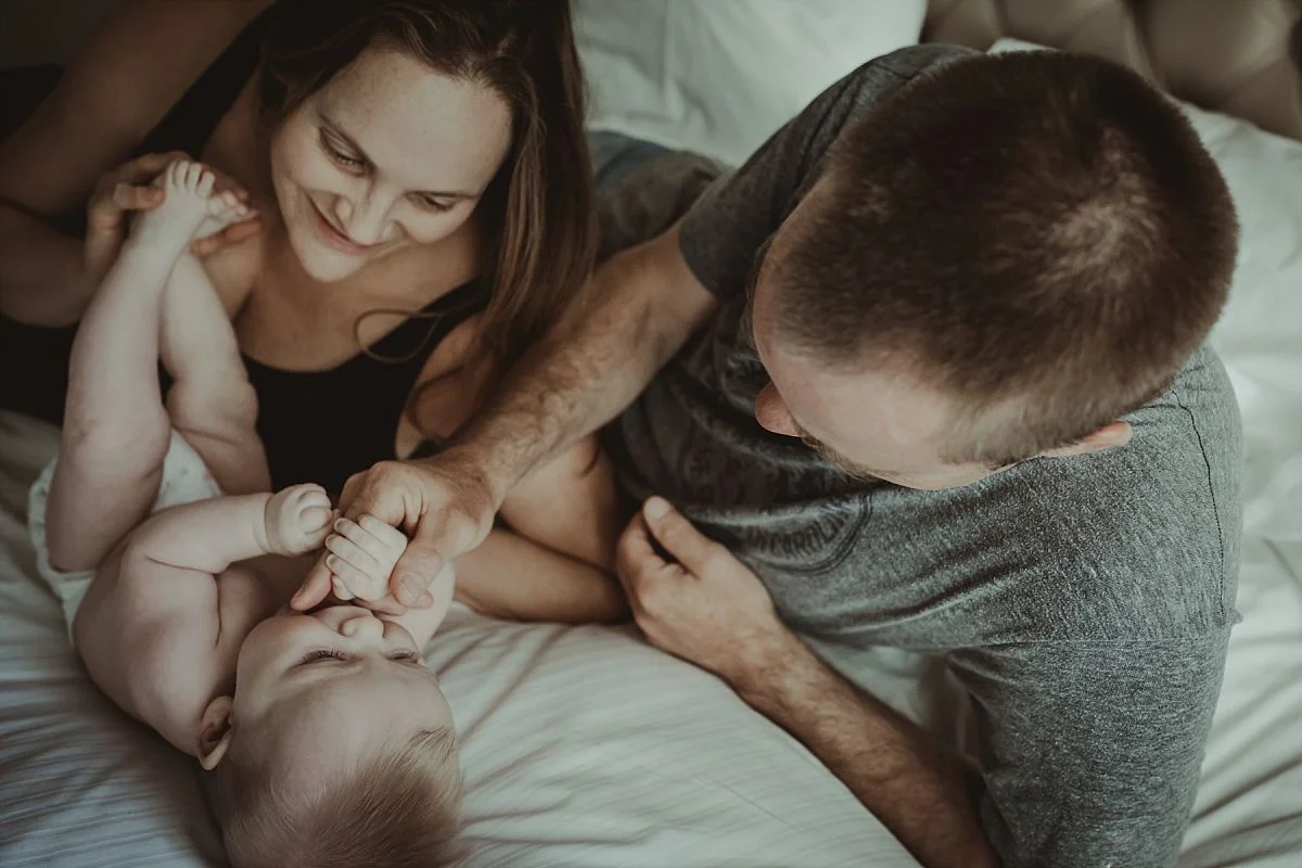 nyc newborn and family photographer mom and dad on bed with baby