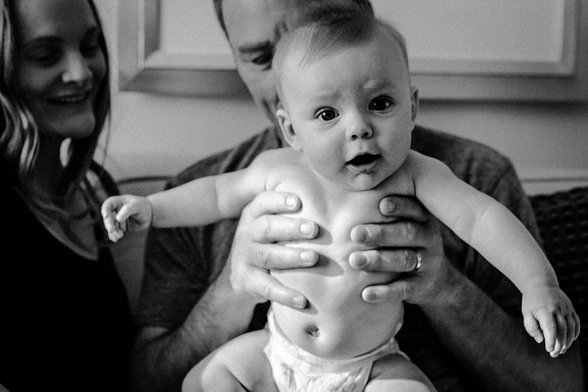 nyc newborn and family photographer dad holding baby with mom on couch