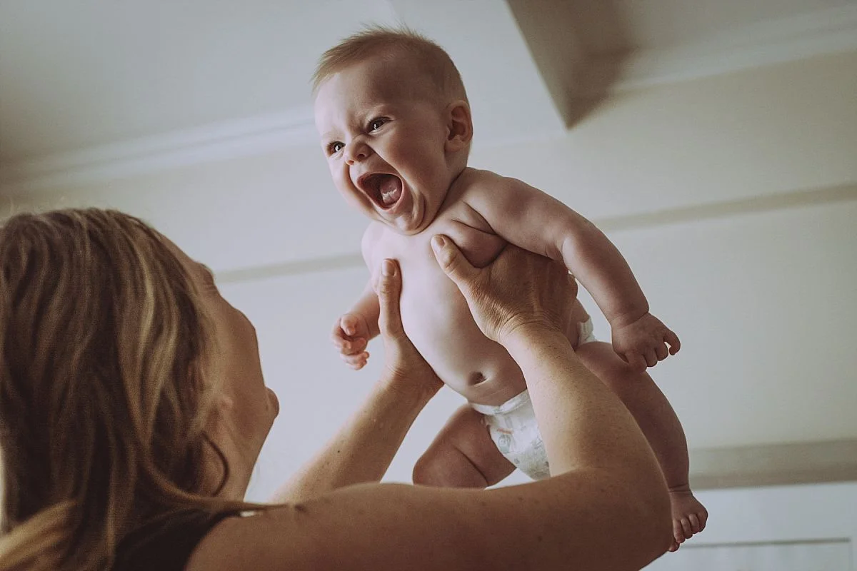 nyc newborn and family photographer mom holding baby in air with very excited look