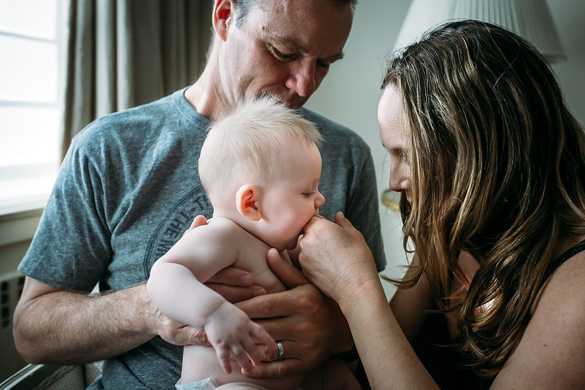 nyc newborn and family photographer baby on dad's lap chewing mom's hand