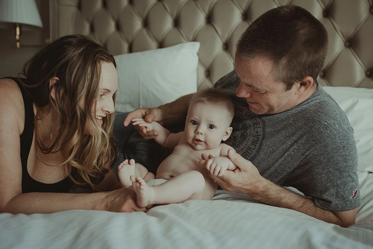 nyc newborn and family photographer mom, dad and baby having fun on hotel bed