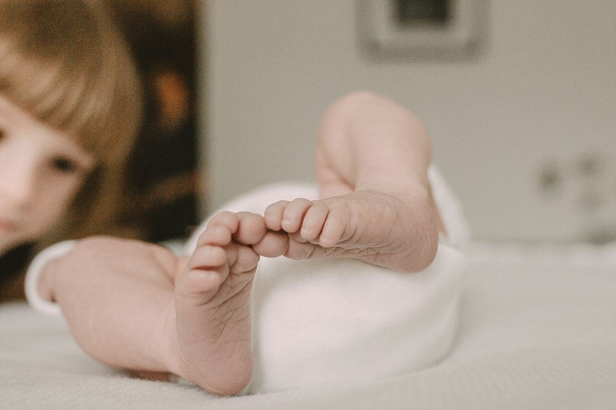 nyc family and newborn photographer big sister looks at newborn sister feet