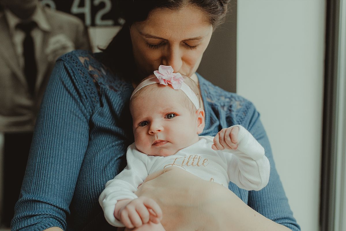 nyc family and newborn photographer mom holding newborn by window newborn looking at camera