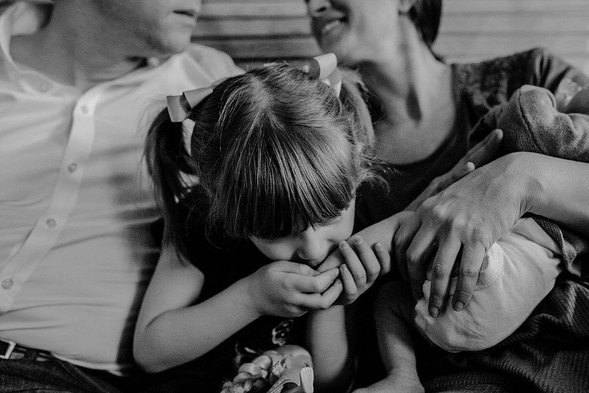 nyc family and newborn photographer big sister kisses newborn feet on could while mom holding