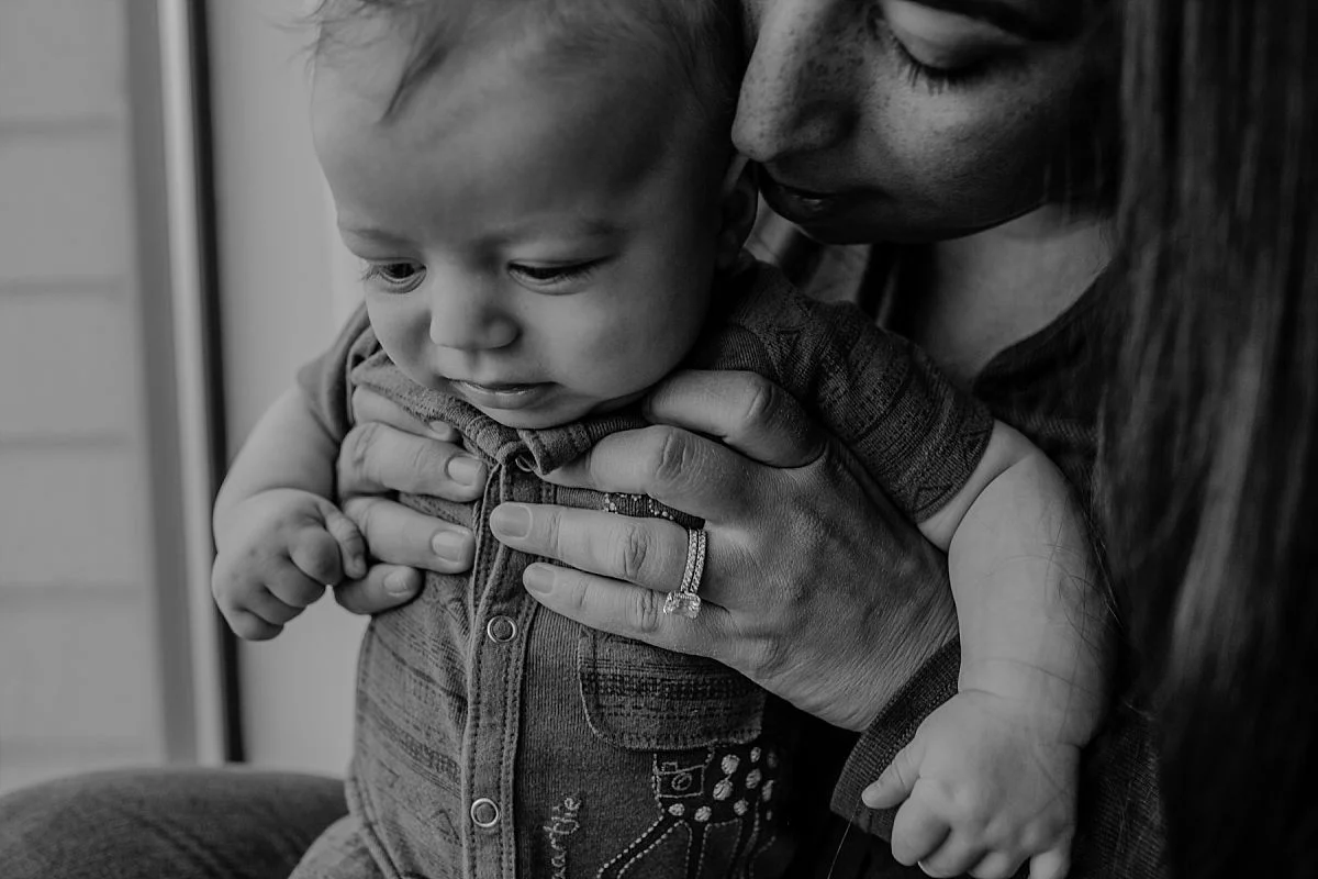 nyc family and newborn photographer mom kisses newborn toddler son near window