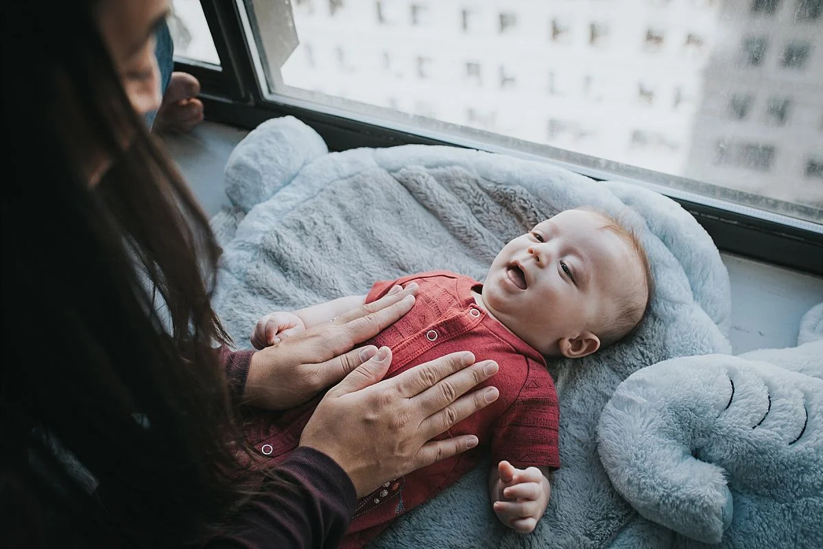 nyc family and newborn photographer newborn baby boy looks playfully at mum while laying on elephant blanket