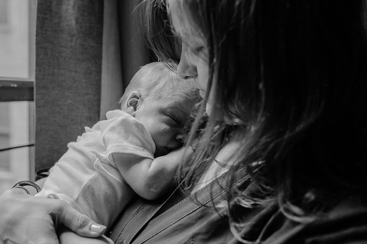 nyc family and newborn photographer Israeli mom holds sleeping newborn boy near window
