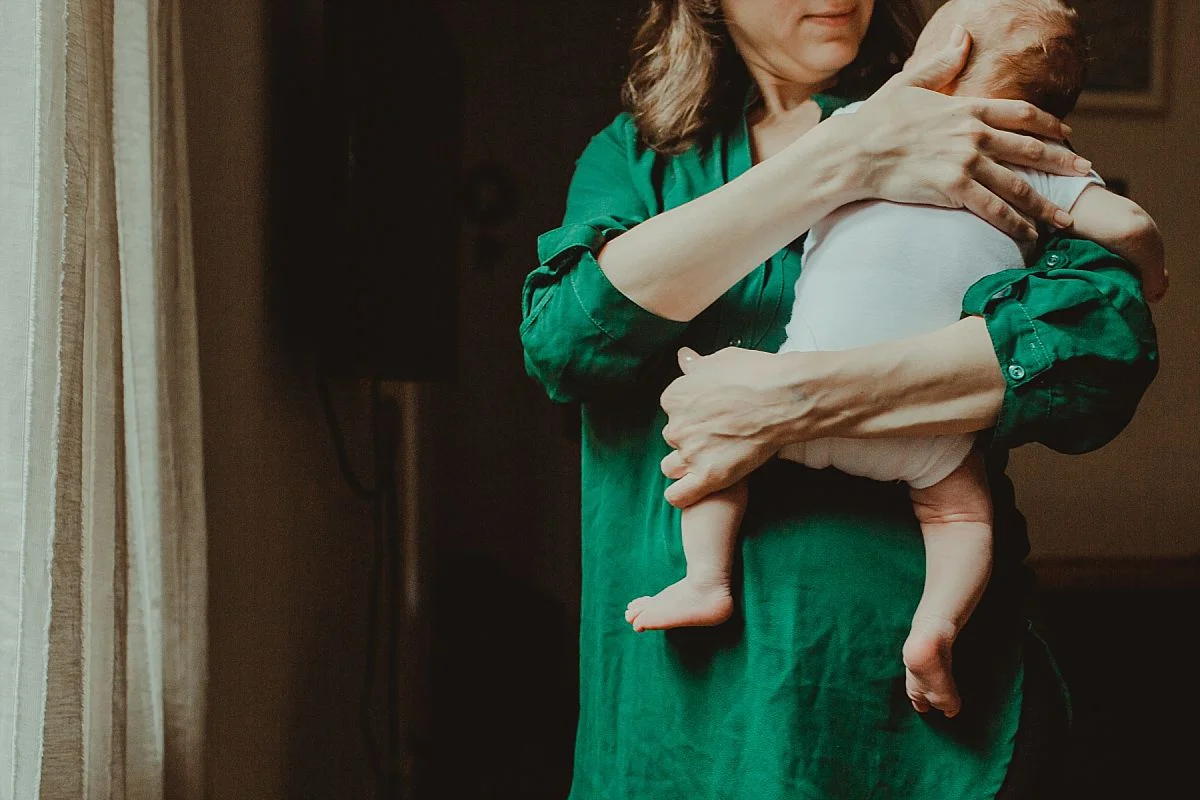 nyc family and newborn photographer mom holds newborn son in bedroom with feet dangling