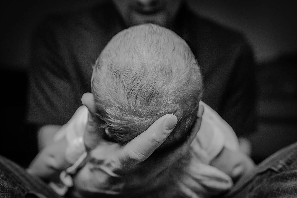 nyc family and newborn photographer dad cups newborn son's head in his lap