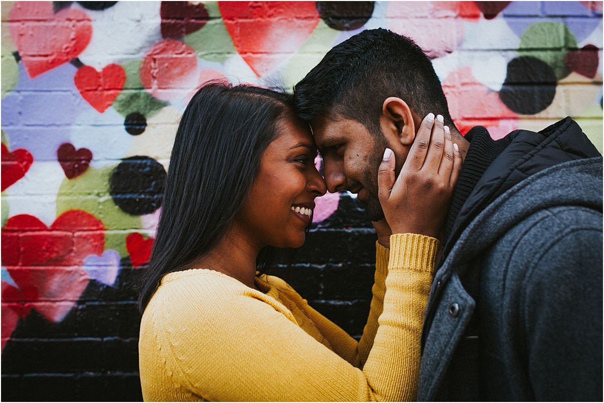 nyc family and newborn photographer expecting husband and wife touch heads in front of graffiti wall