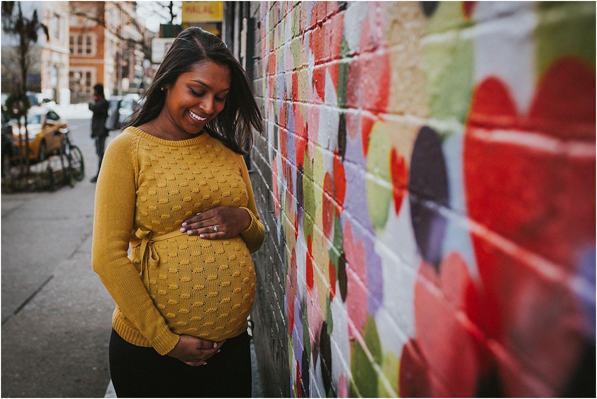 nyc family and newborn photographer expecting mom holds baby bump in front of East Village graffiti wall