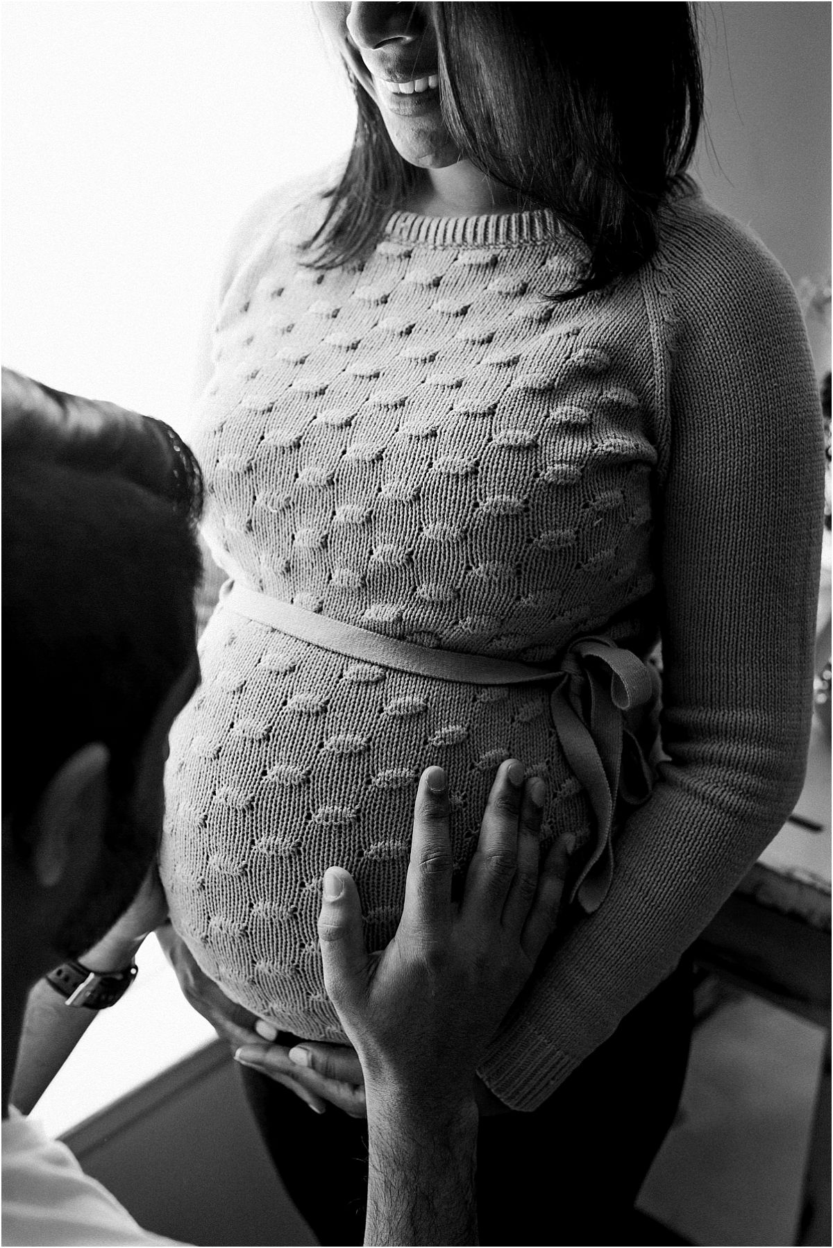 nyc family and newborn photographer husband holds expecting mom's belly in front of light filled window