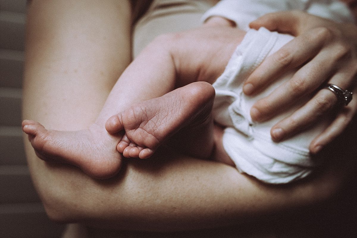 nyc family and newborn photographer new mom holds sleeping newborn baby girl newborn feet dangle from mom's arms