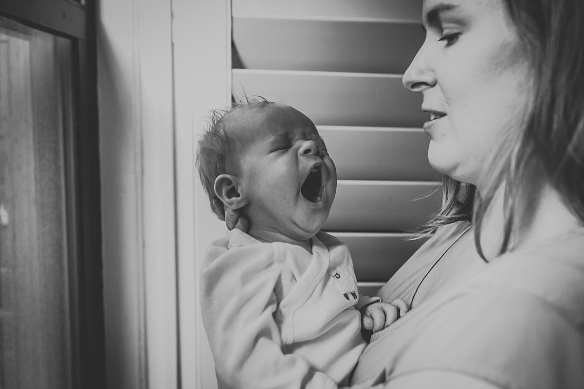 nyc family and newborn photographer mom holds yawning baby girl in apartment by window